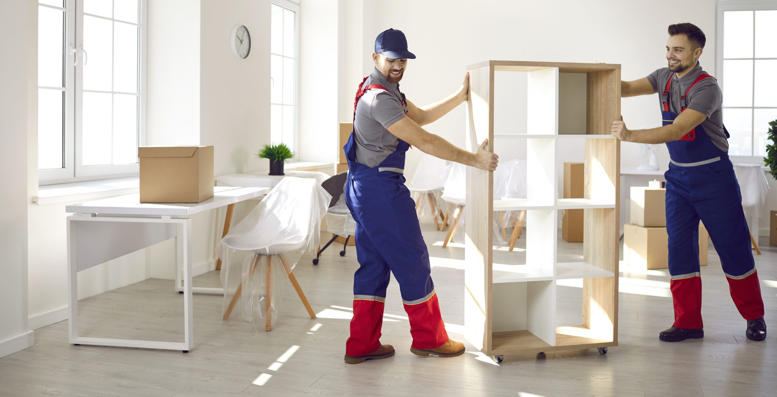 Two movers carrying shelving unit in empty room